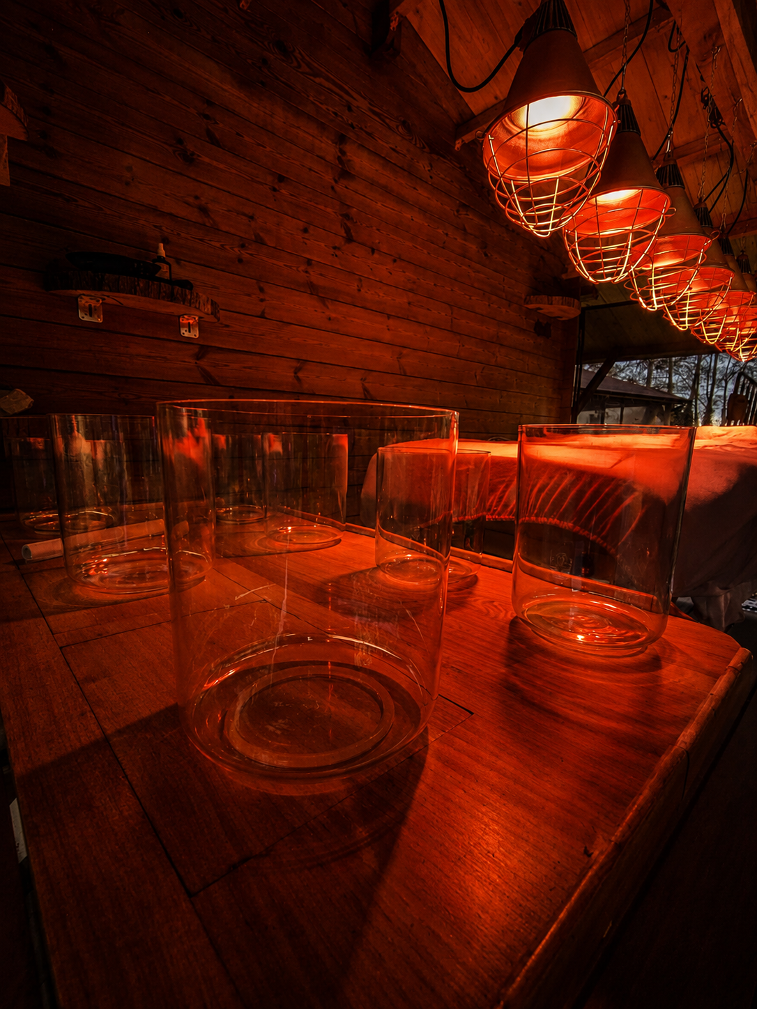Zeven klankschalen van glas op een houten tafel in warm rood licht in de behandelruimte