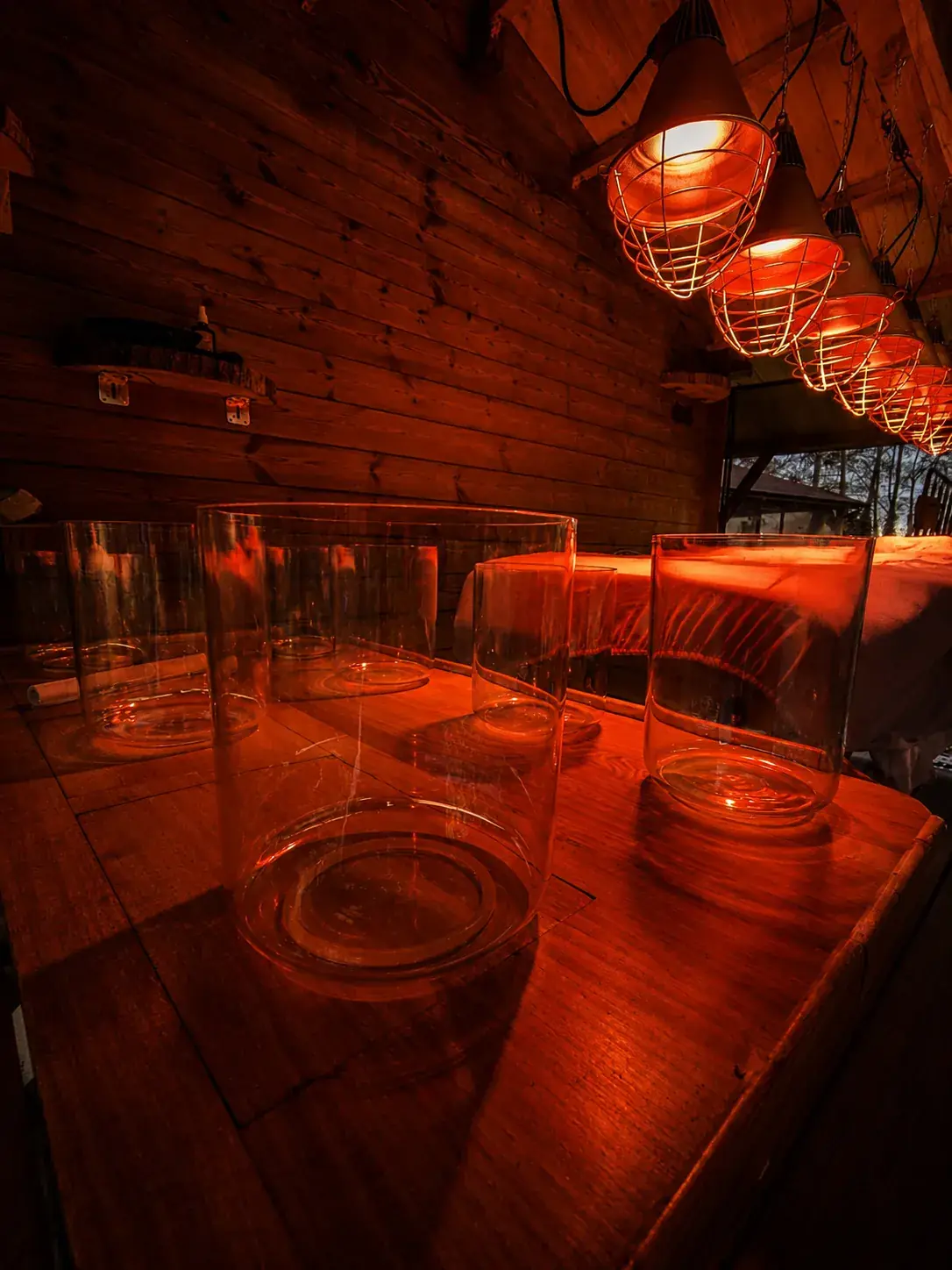Zeven klankschalen van glas op een houten tafel in warm rood licht in de behandelruimte